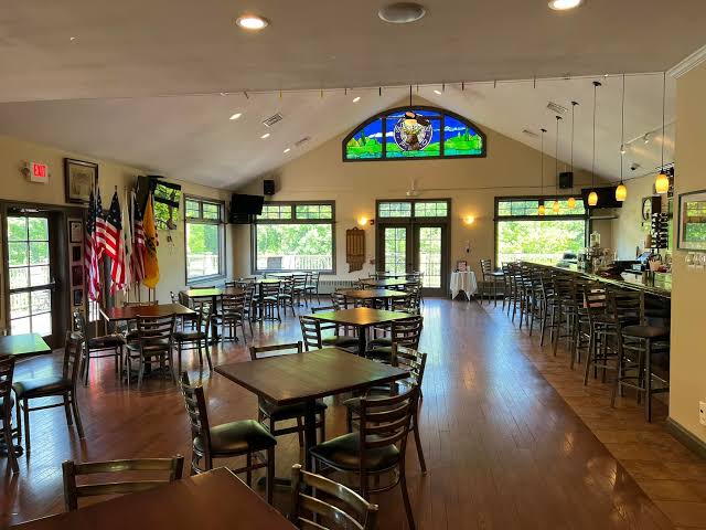 Inside the Danbury Elks Lodge, showing the bar, dining tables, and stained-glass Elks emblem window